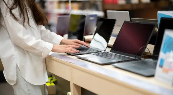 Kobieta w białej koszuli testuje laptopy na wystawie sklepowej.